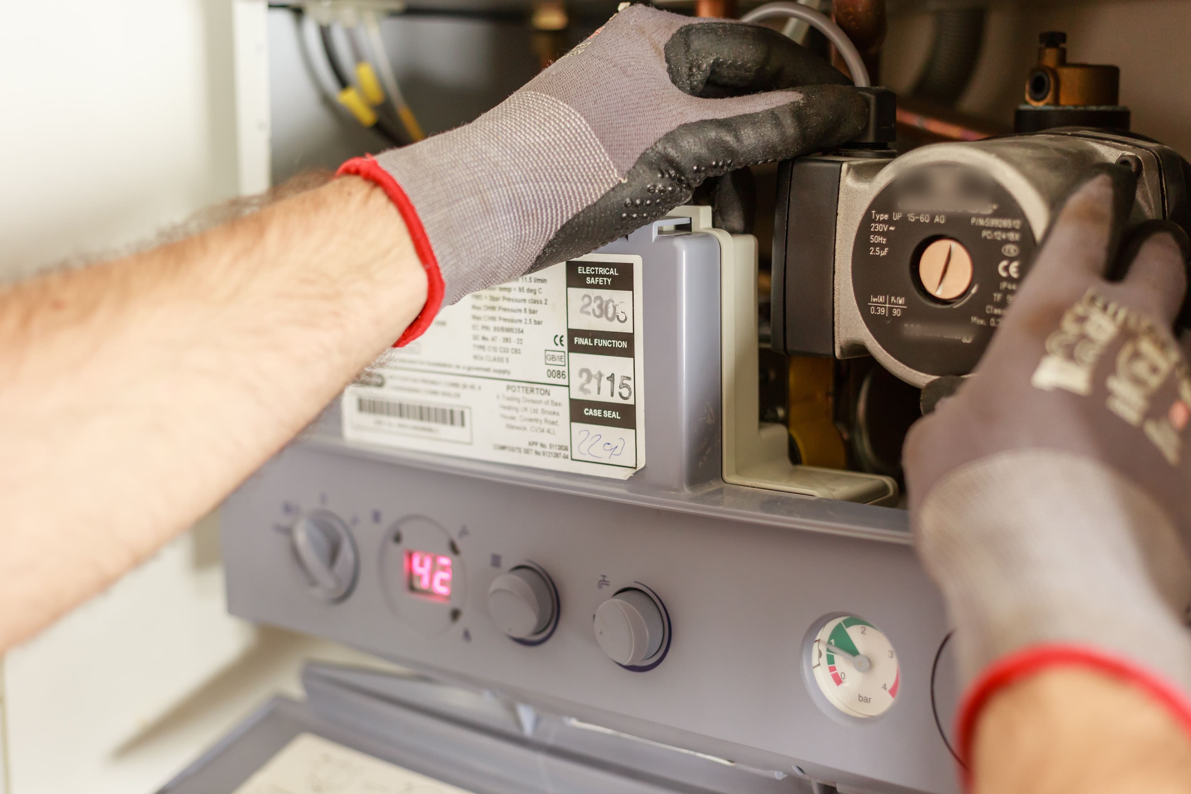 Technician's gloved hand inspecting a circulator pump on a heating system